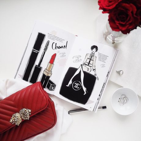 Flatlay s obrázkem z knížky o Chanel, rudými růžemi a červenou crossbody kabelkou