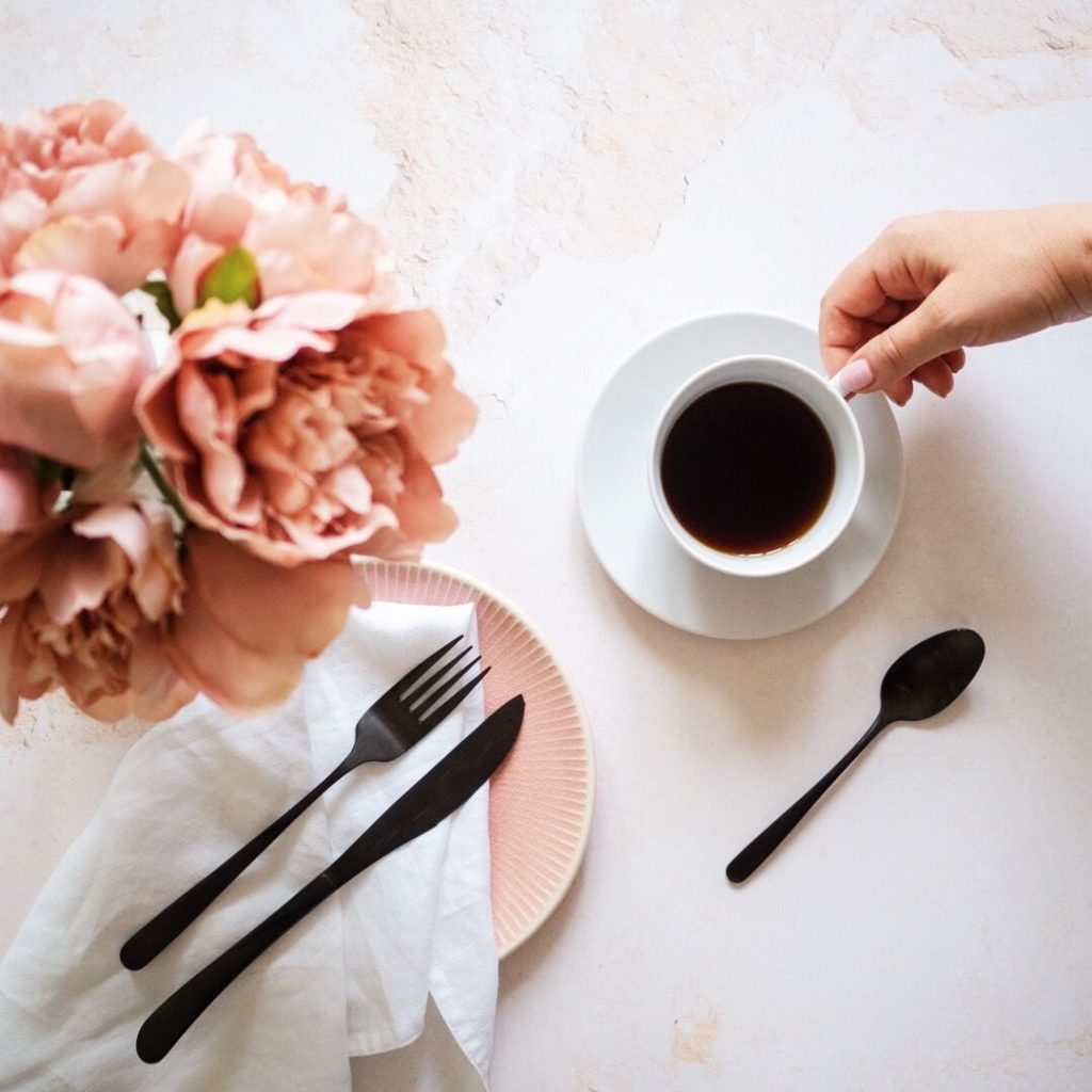 Flatlay fotka s kávou, černými příbory a květinou